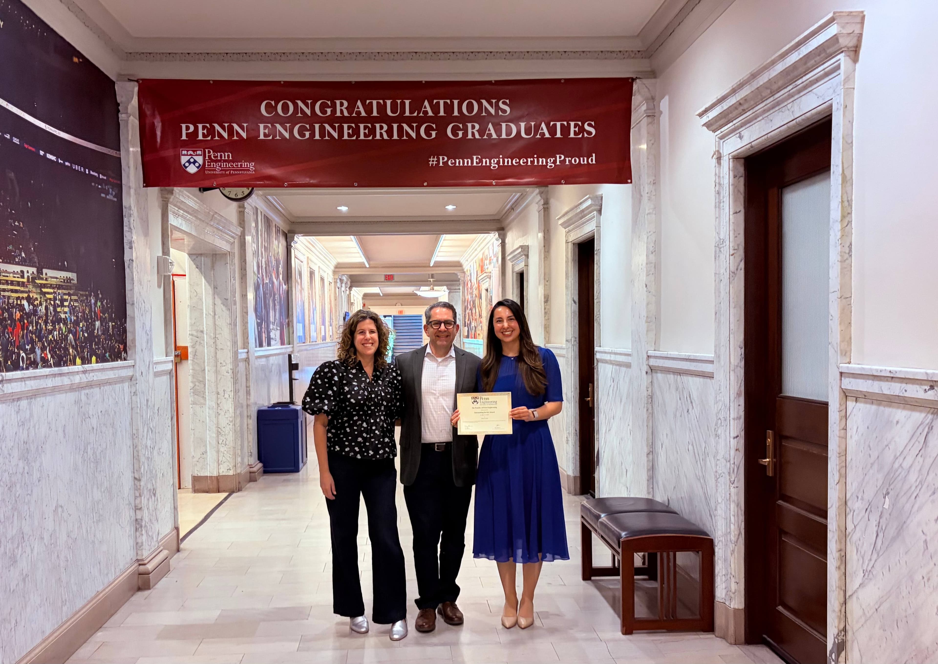 Sofia El Amrani holding her Outstanding Service Award certificate with Professors Sarah Rottenberg and Jeffrey Babin under a Penn Engineering graduation banner